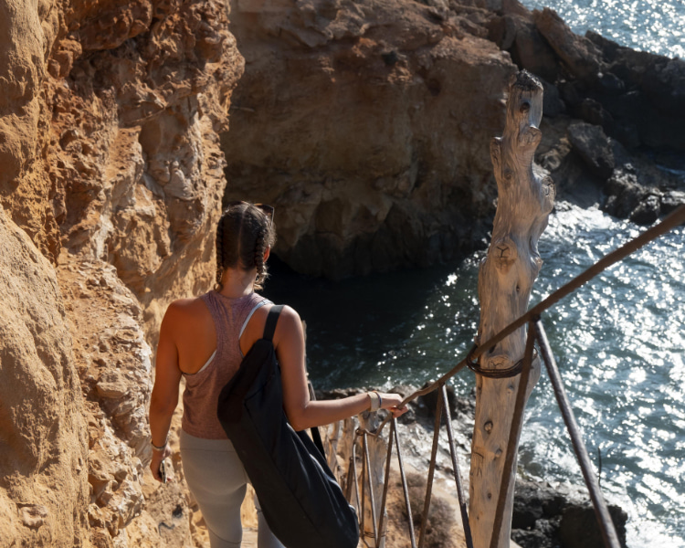 A person walking down the stairs towards the turquoise blue sea.